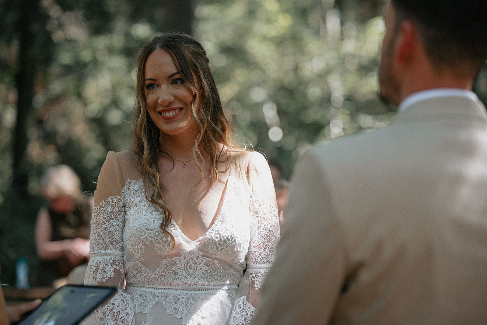 A bride and groom are getting married in the woods and the bride is smiling at the groom.