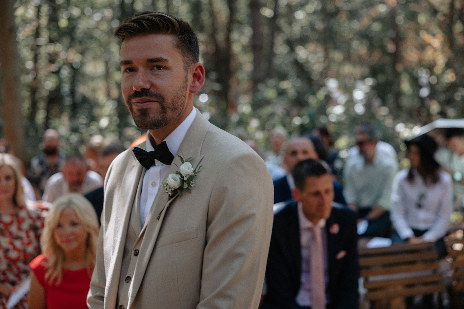 A man in a suit and bow tie is standing in front of a crowd of people at a wedding ceremony.