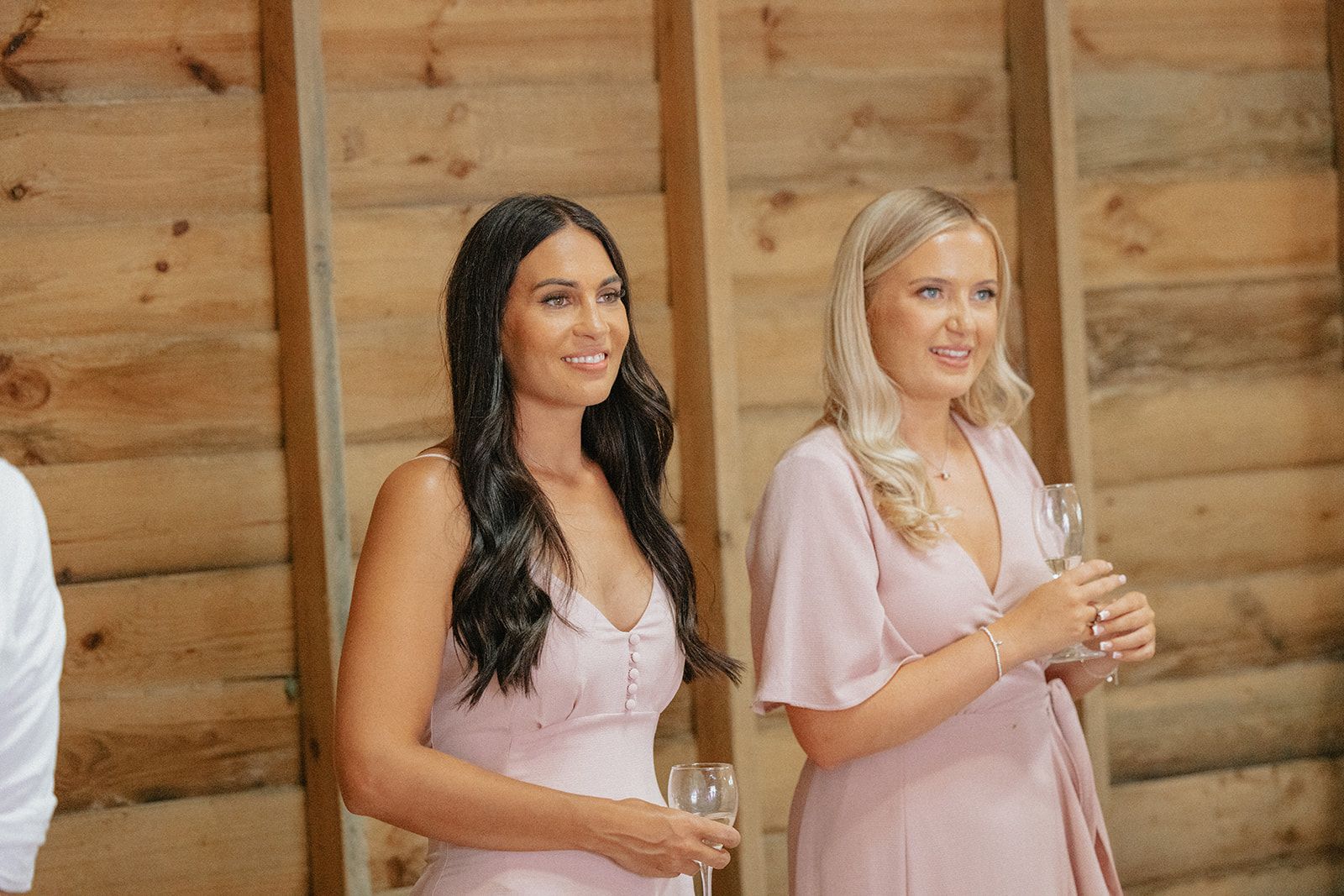 Two women in pink dresses are standing next to each other holding wine glasses.