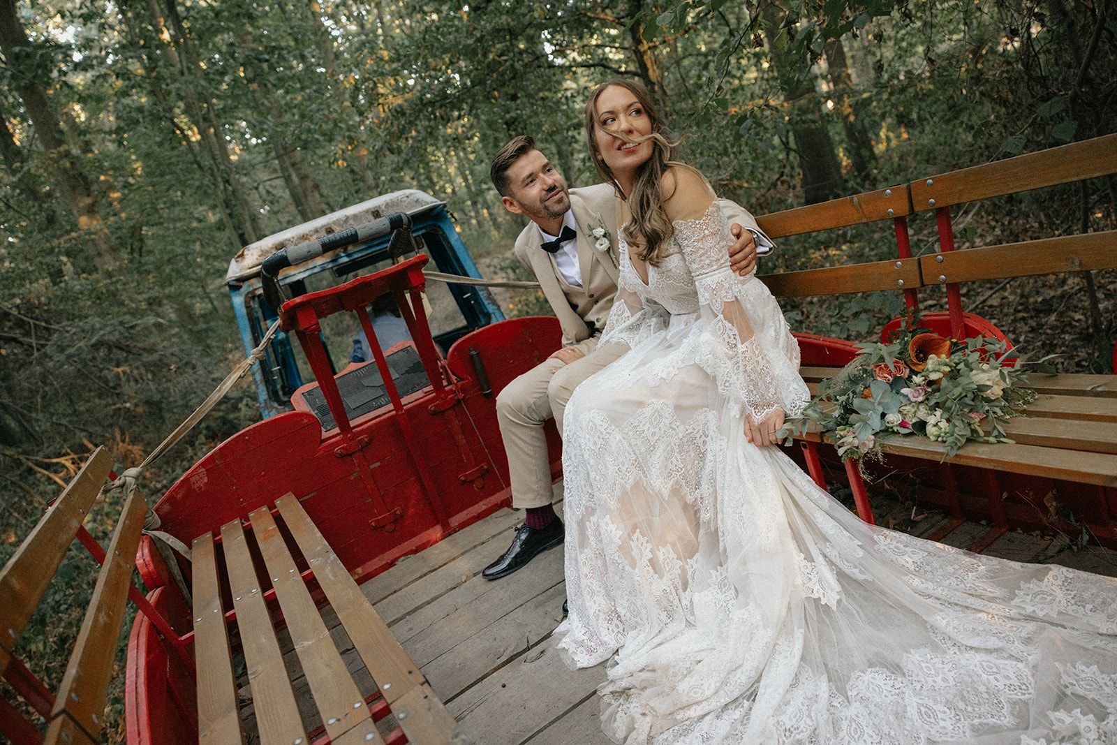 A bride and groom are posing for a picture in a wagon in the woods.