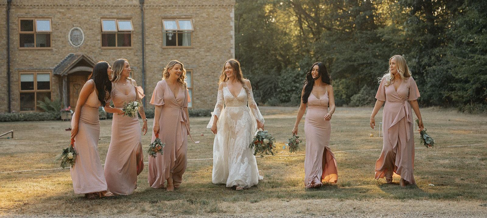 A bride and her bridesmaids are walking in front of a brick building.
