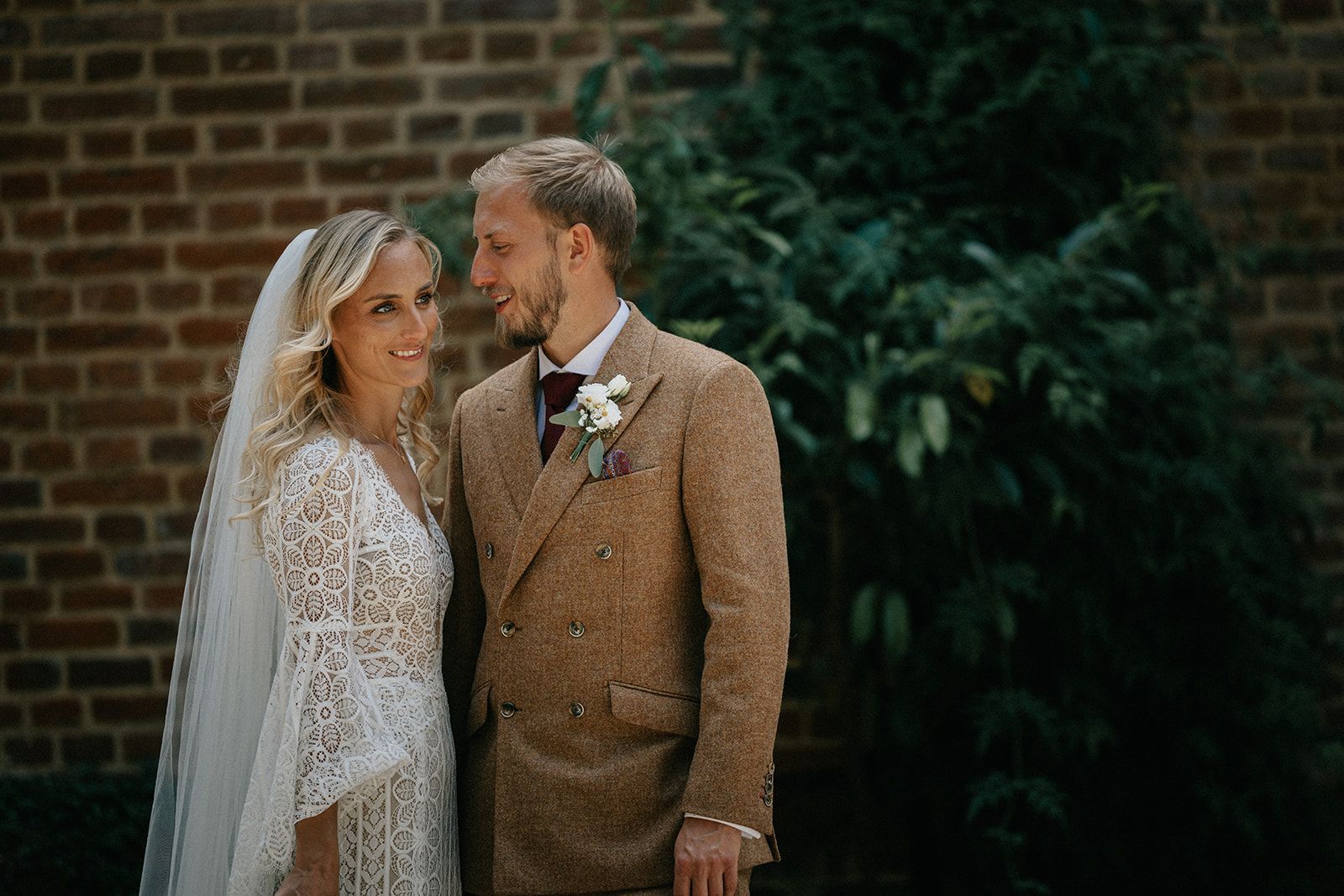 A bride and groom are standing next to each other in front of a brick wall.