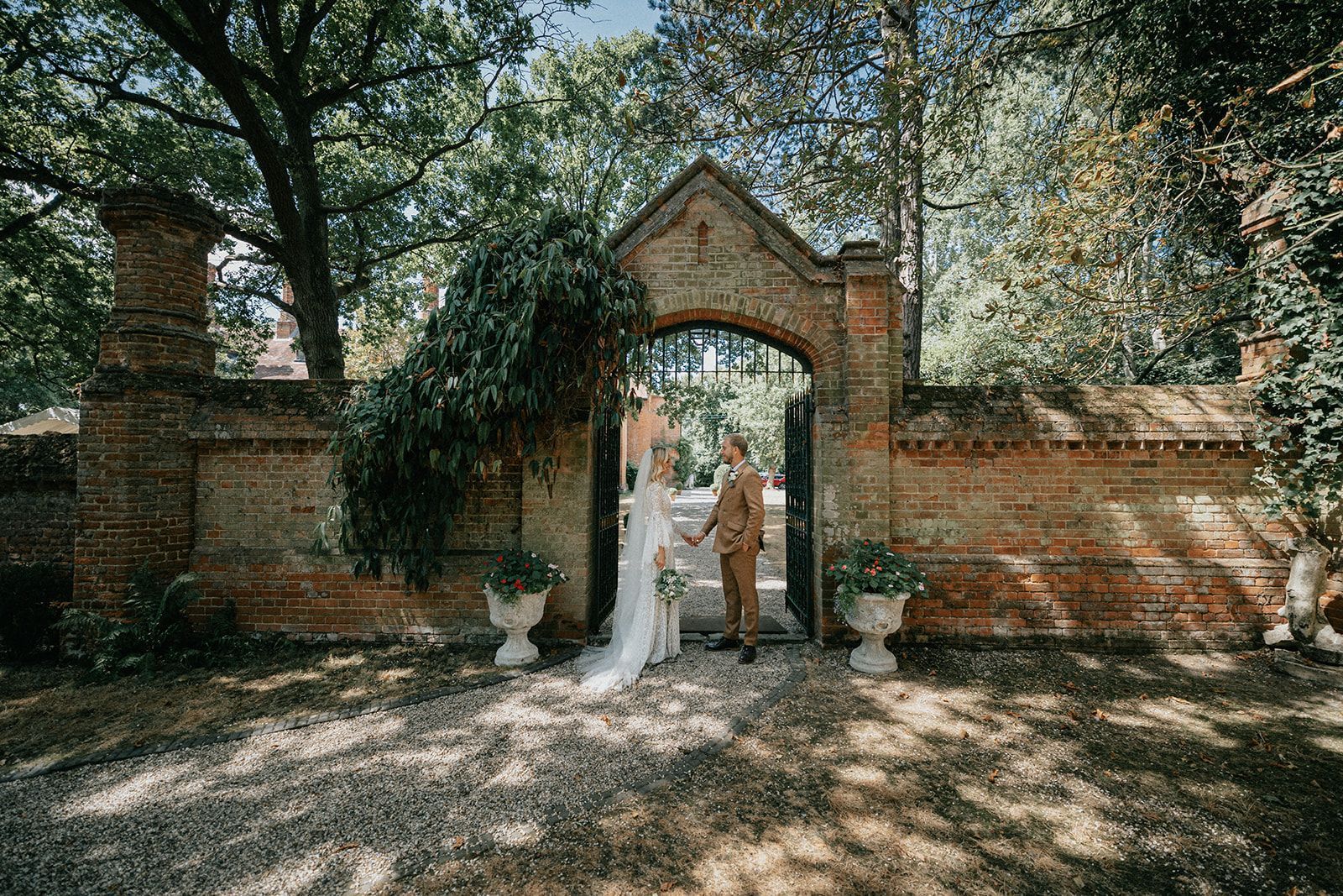 A bride and groom are standing in front of a brick wall holding hands.