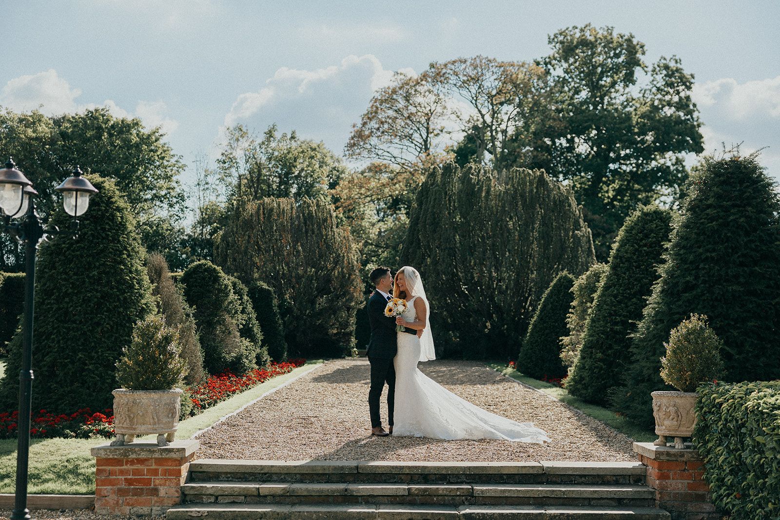 A bride and groom are kissing in a garden on their wedding day.