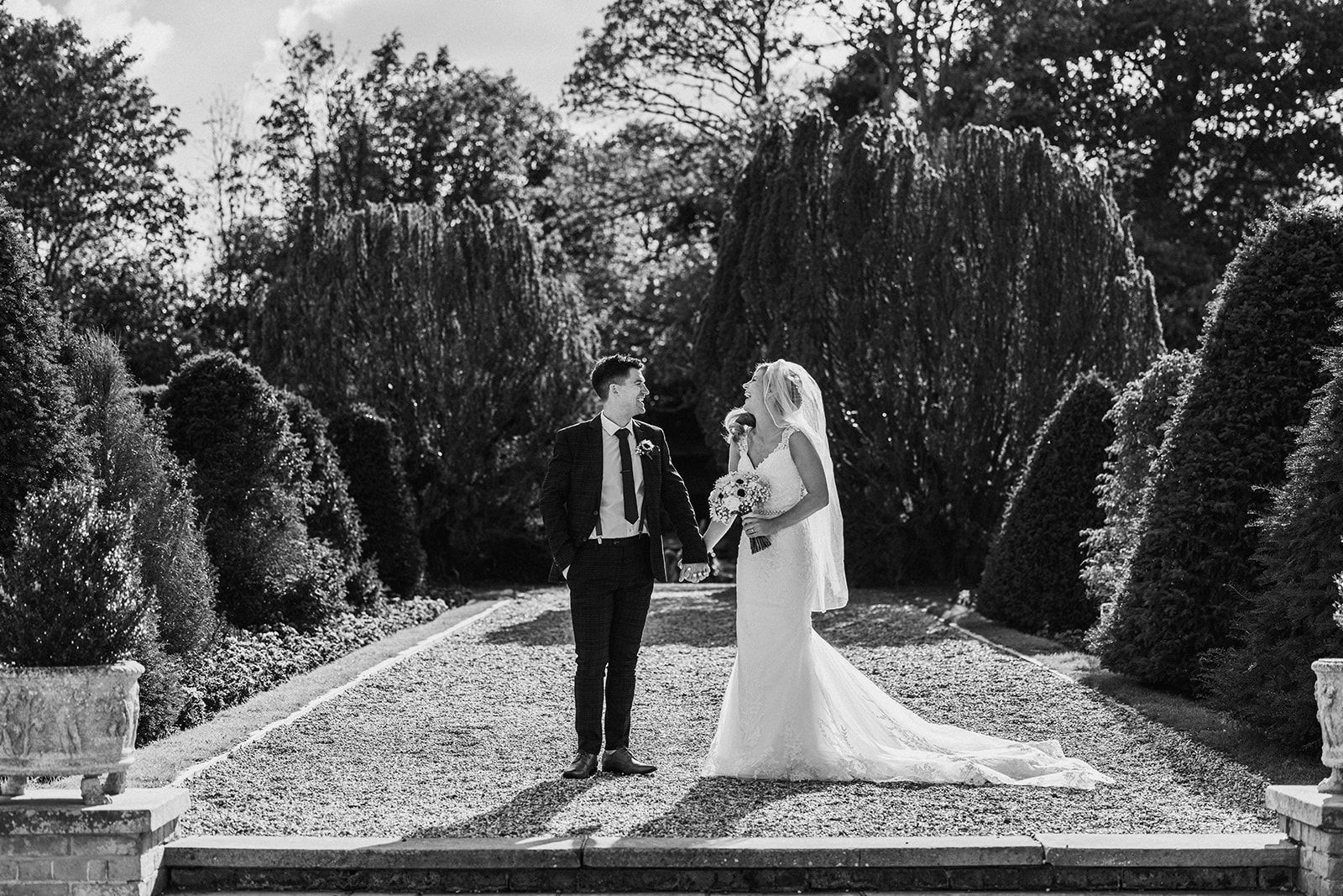 A black and white photo of a bride and groom standing next to each other in a garden.