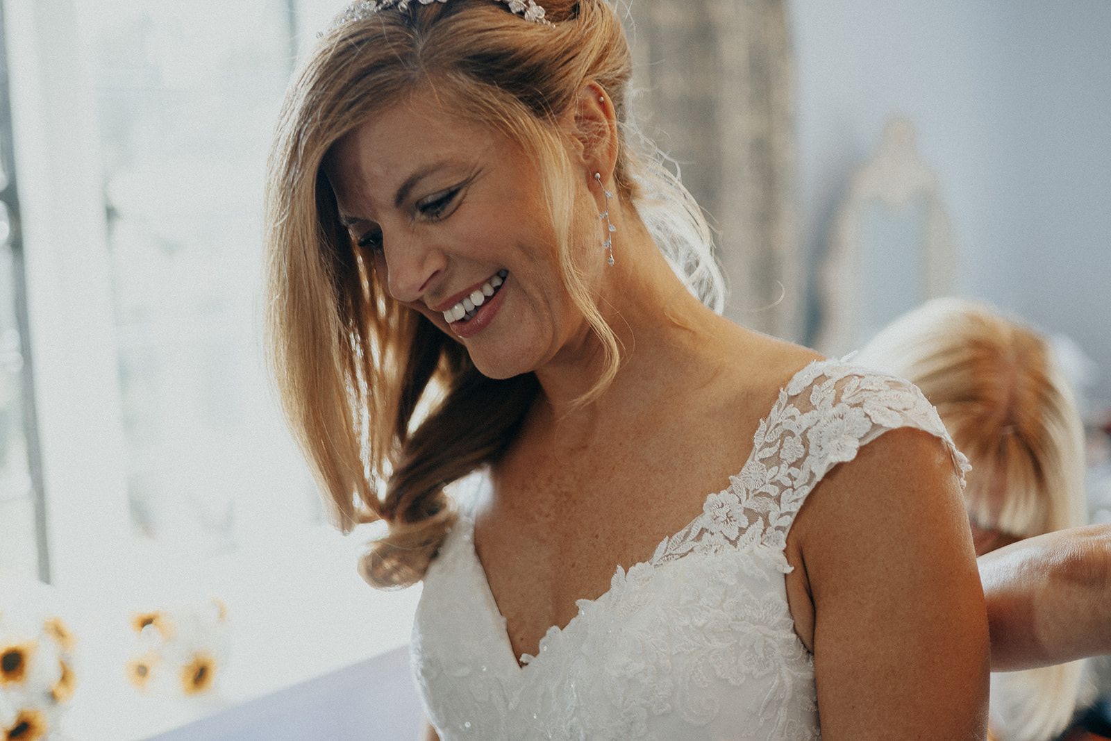 A woman in a wedding dress is smiling while getting ready for her wedding.