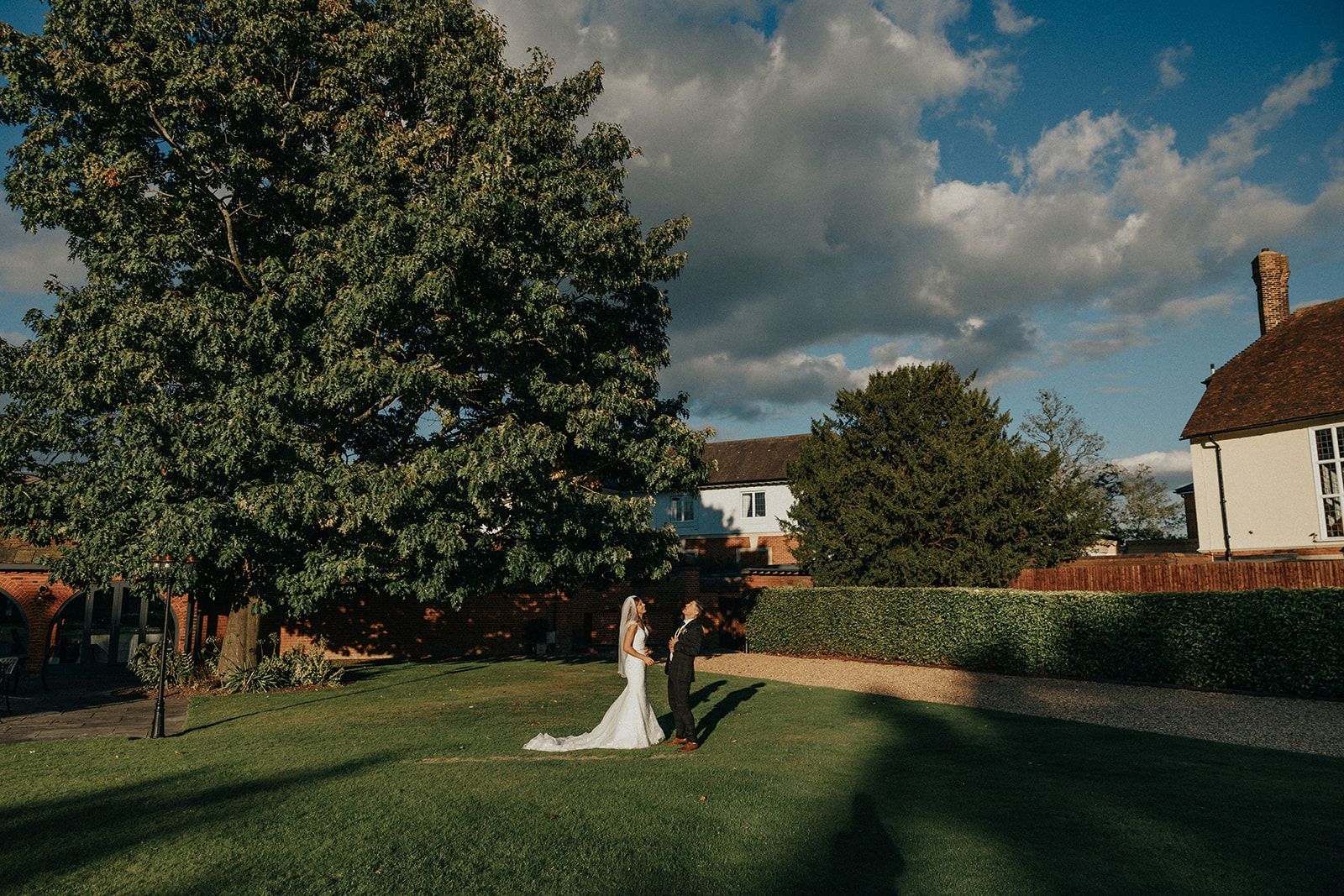 A bride and groom are standing in a grassy field in front of a house.