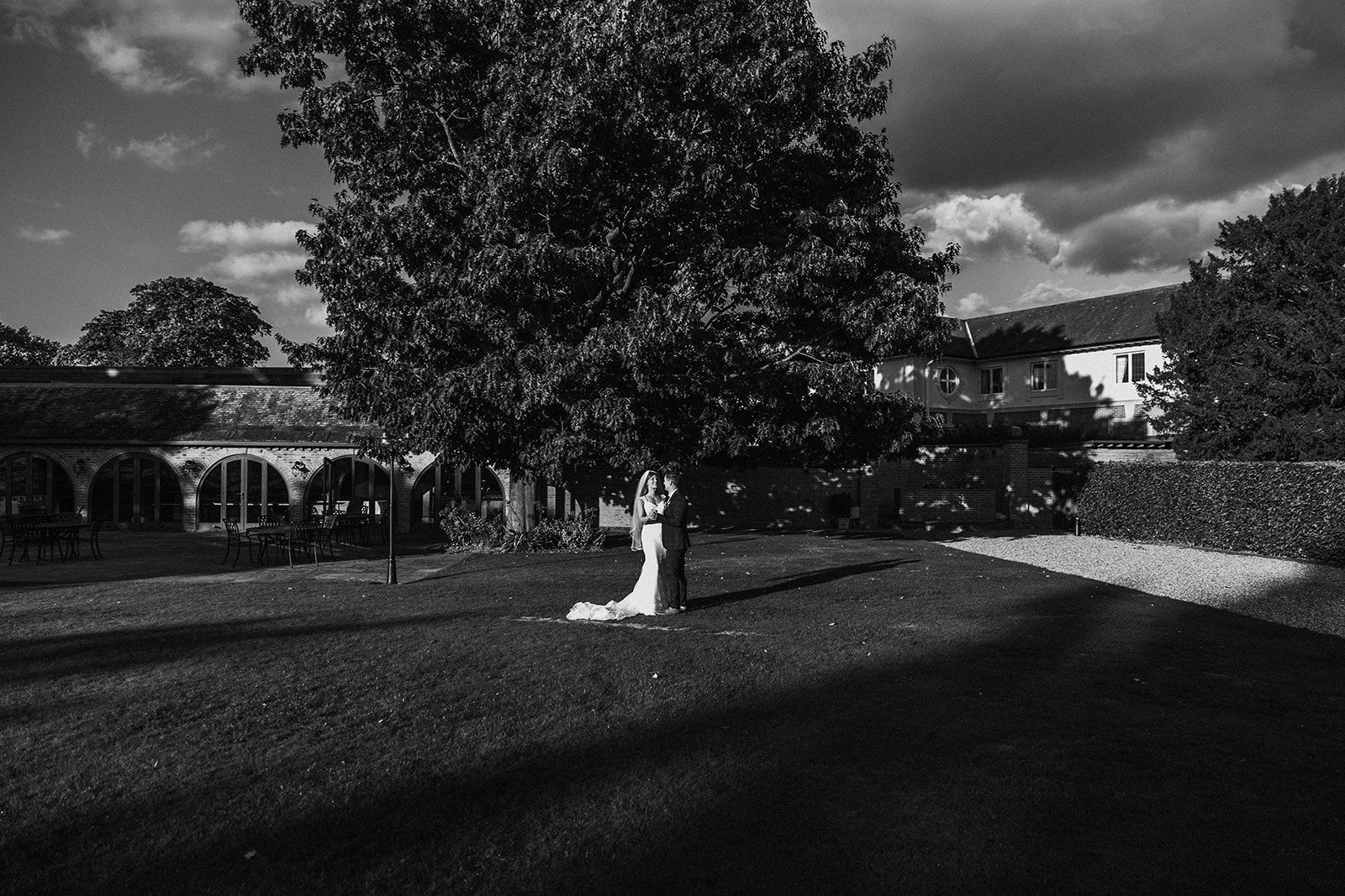 A black and white photo of a bride and groom standing under a tree.