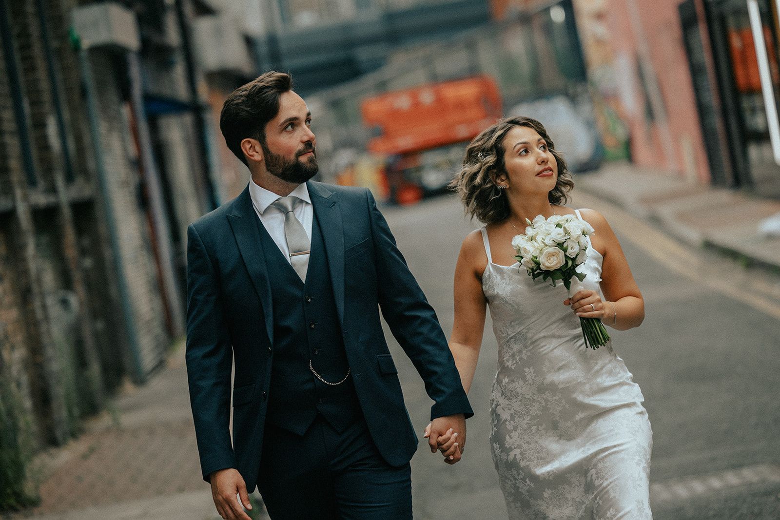 A bride and groom are walking down a city street holding hands.