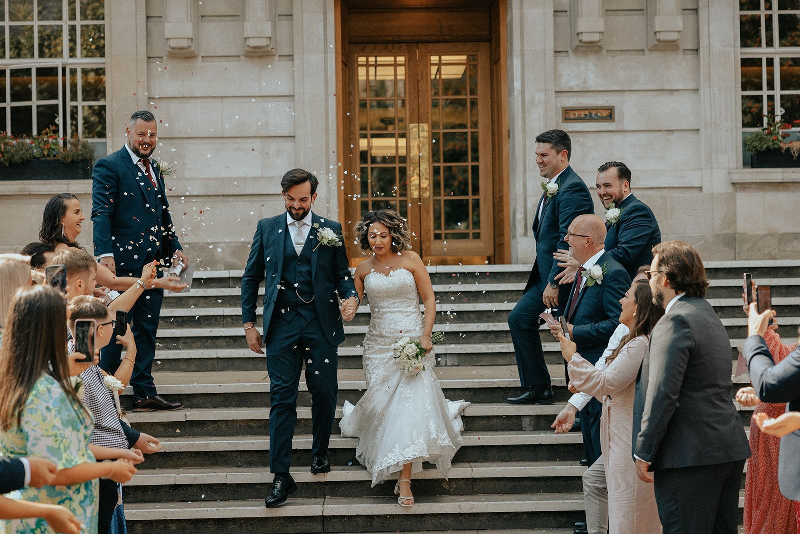 A bride and groom are walking down the stairs of a building surrounded by confetti.