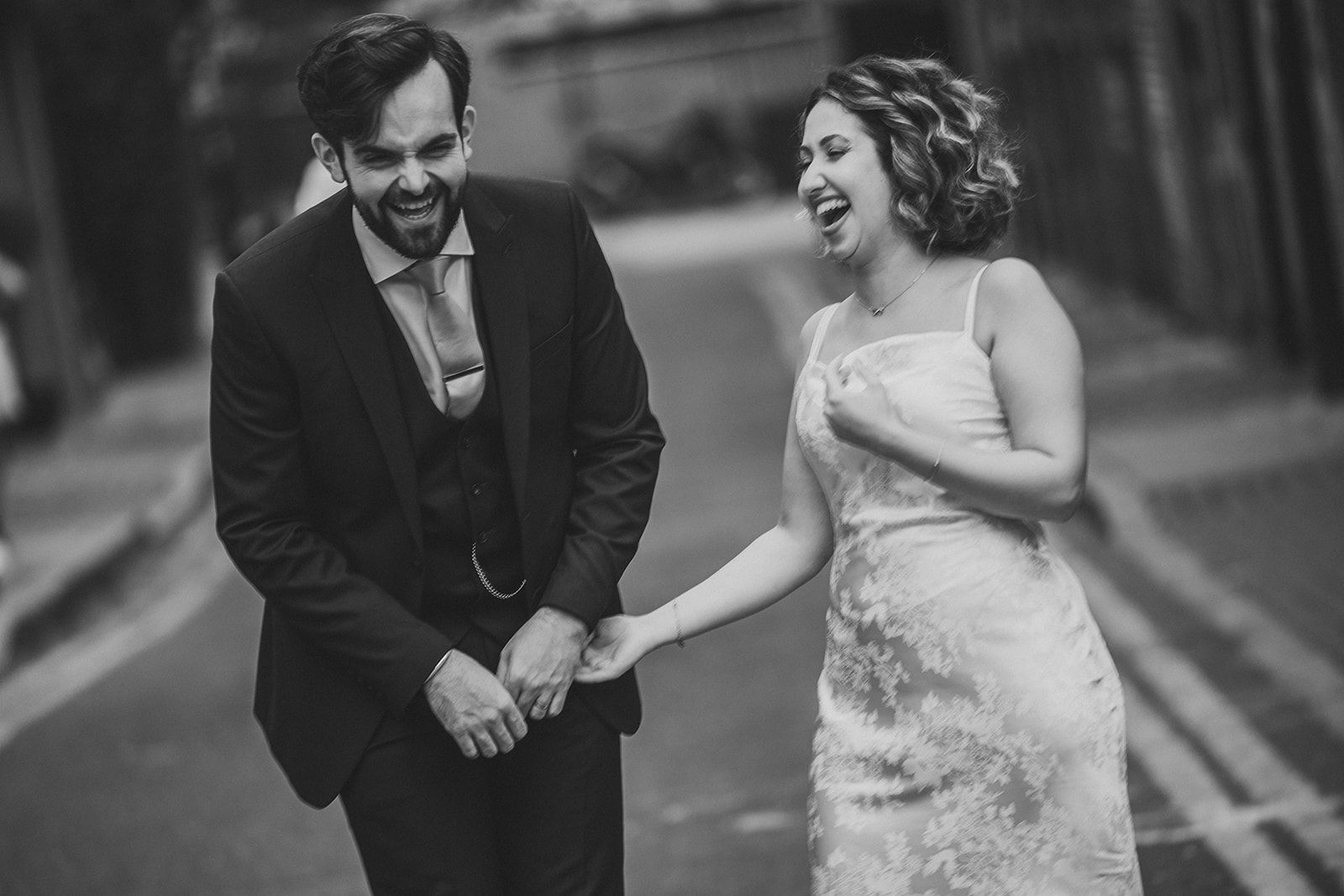 A black and white photo of a bride and groom holding hands on a street.