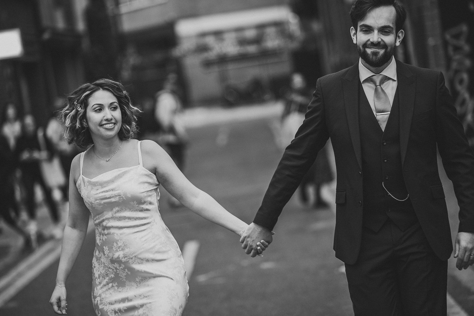 A bride and groom are holding hands while walking down the street.