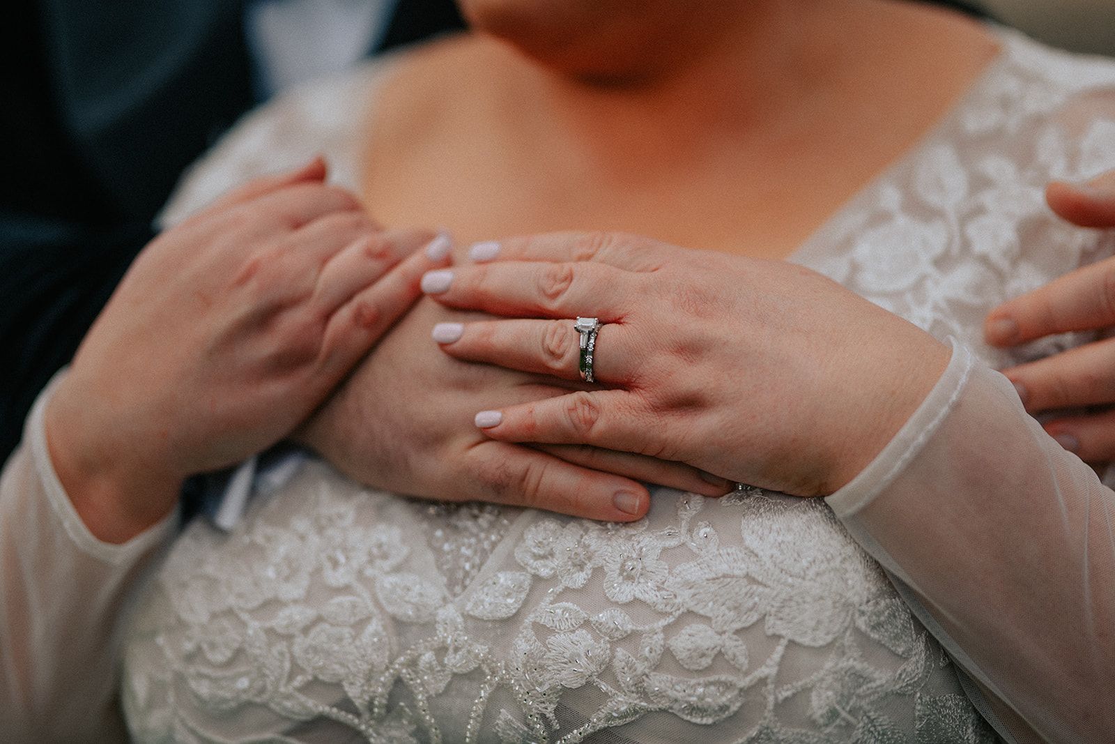 A bride and groom are holding hands and the bride has a wedding ring on her finger.