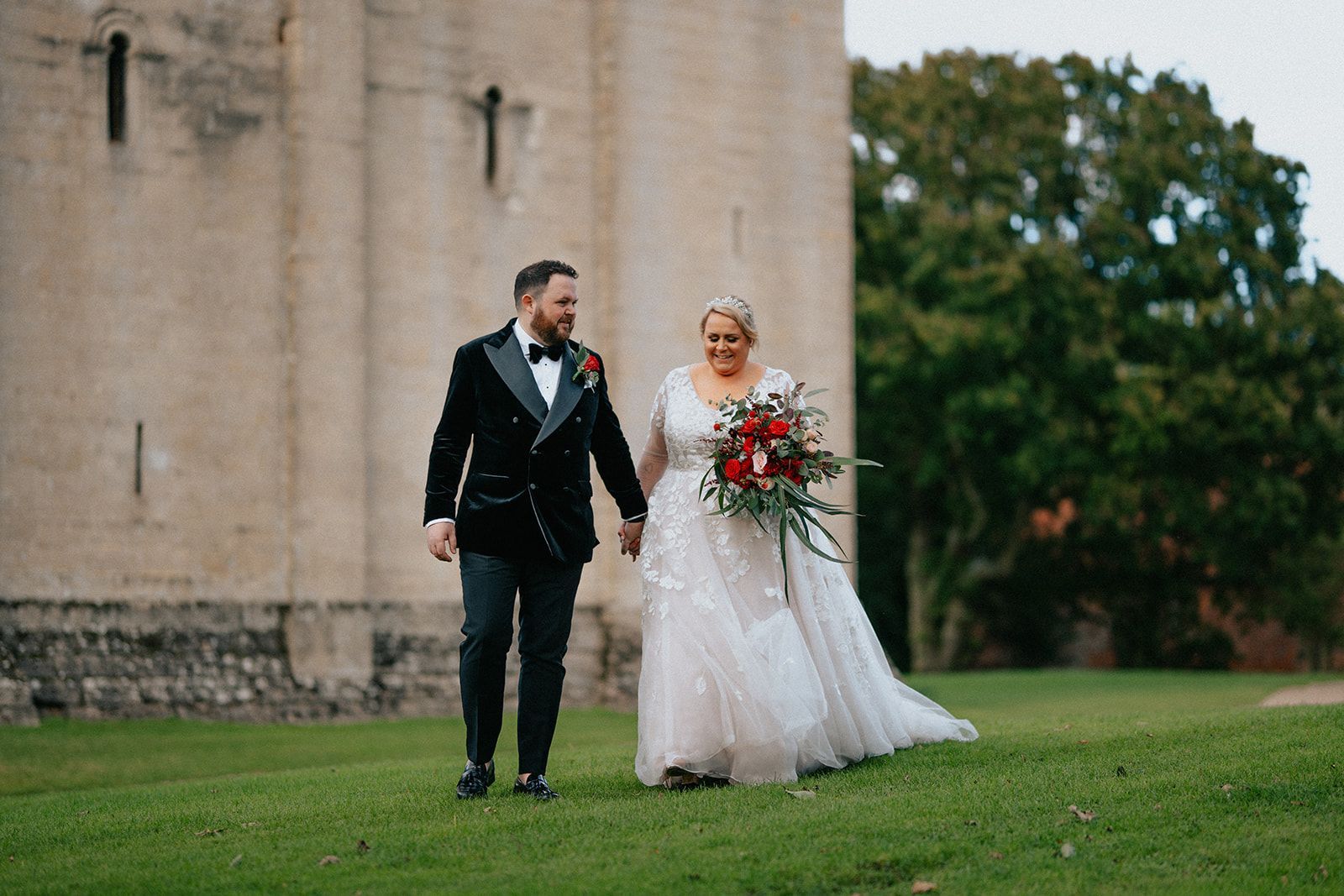 A bride and groom are walking in front of a castle holding hands.