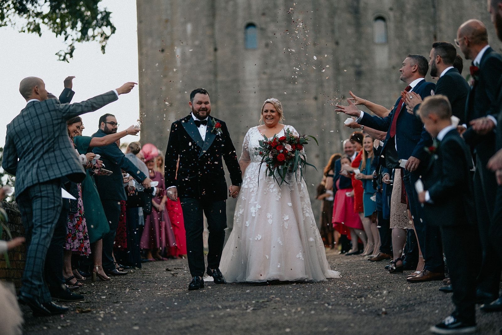 A bride and groom are walking through a crowd of people throwing confetti at them.