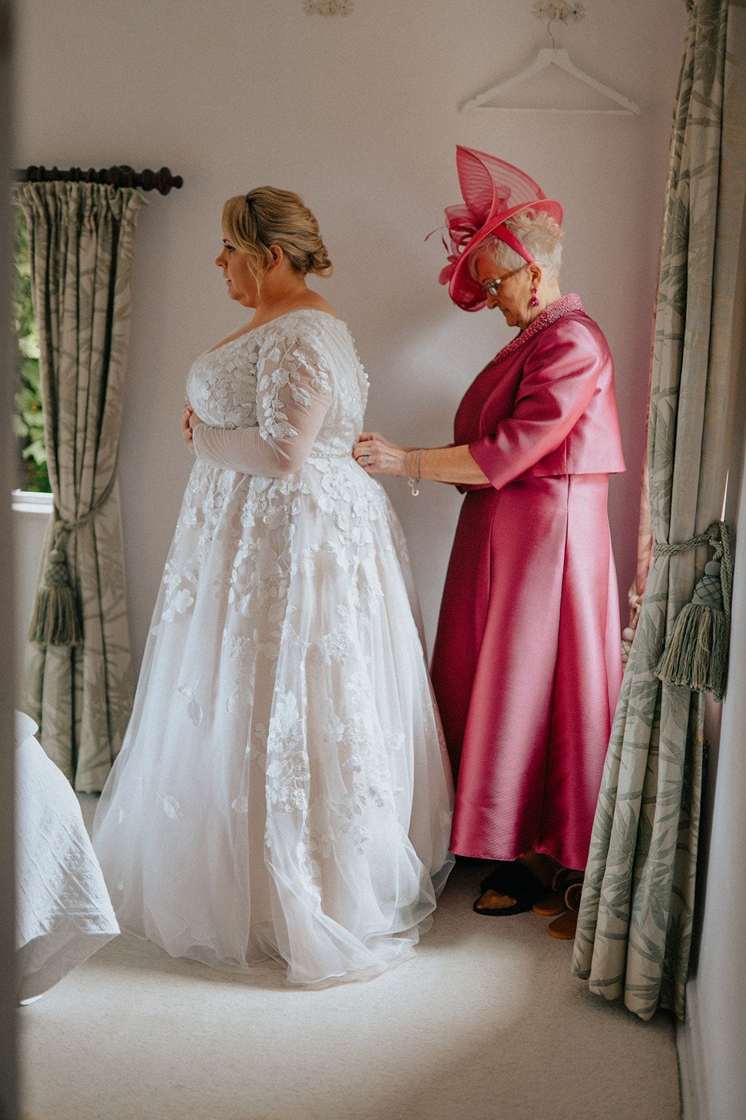 A woman in a pink dress is helping a bride get ready for her wedding.