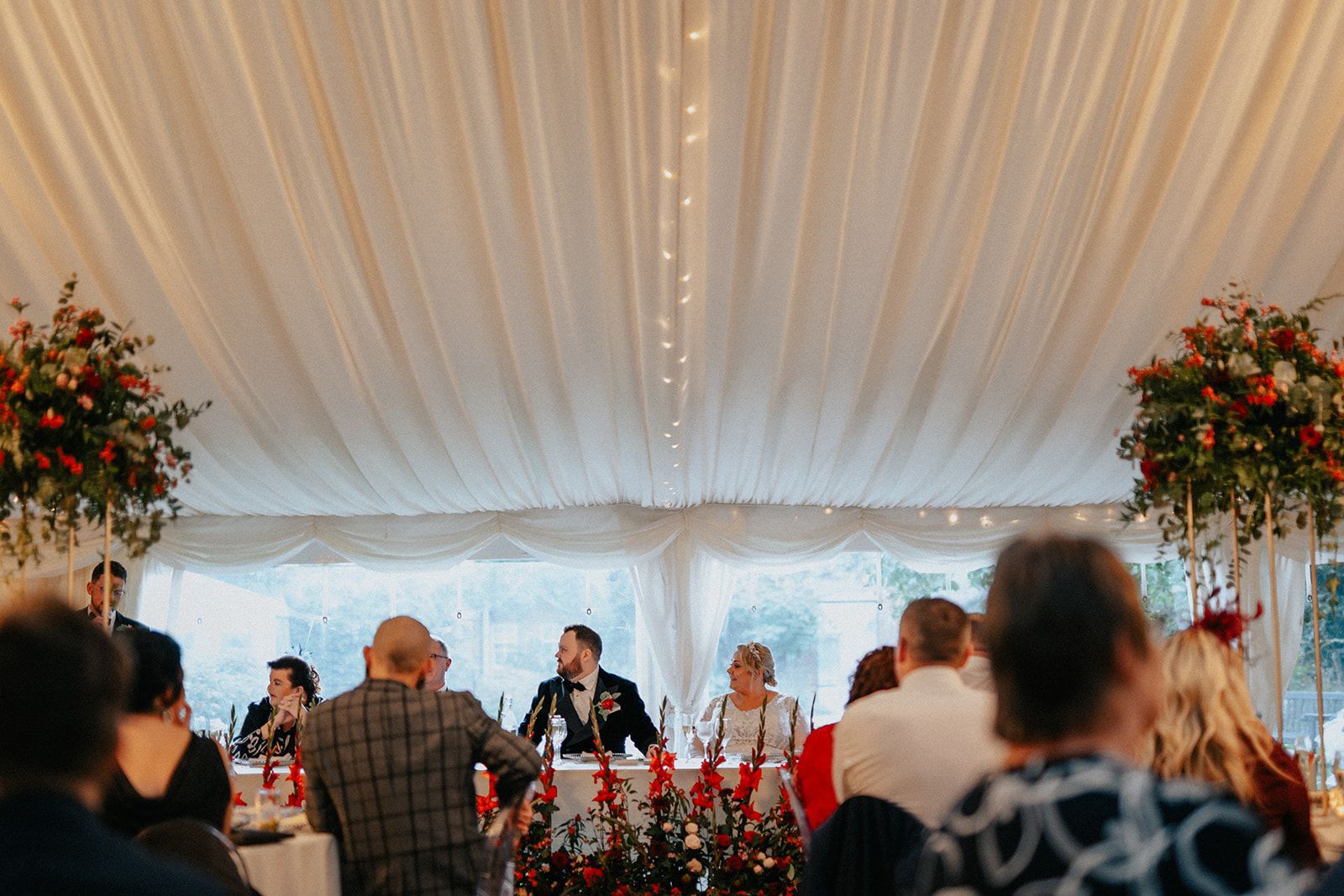 A group of people are sitting at a table under a tent at a wedding reception.