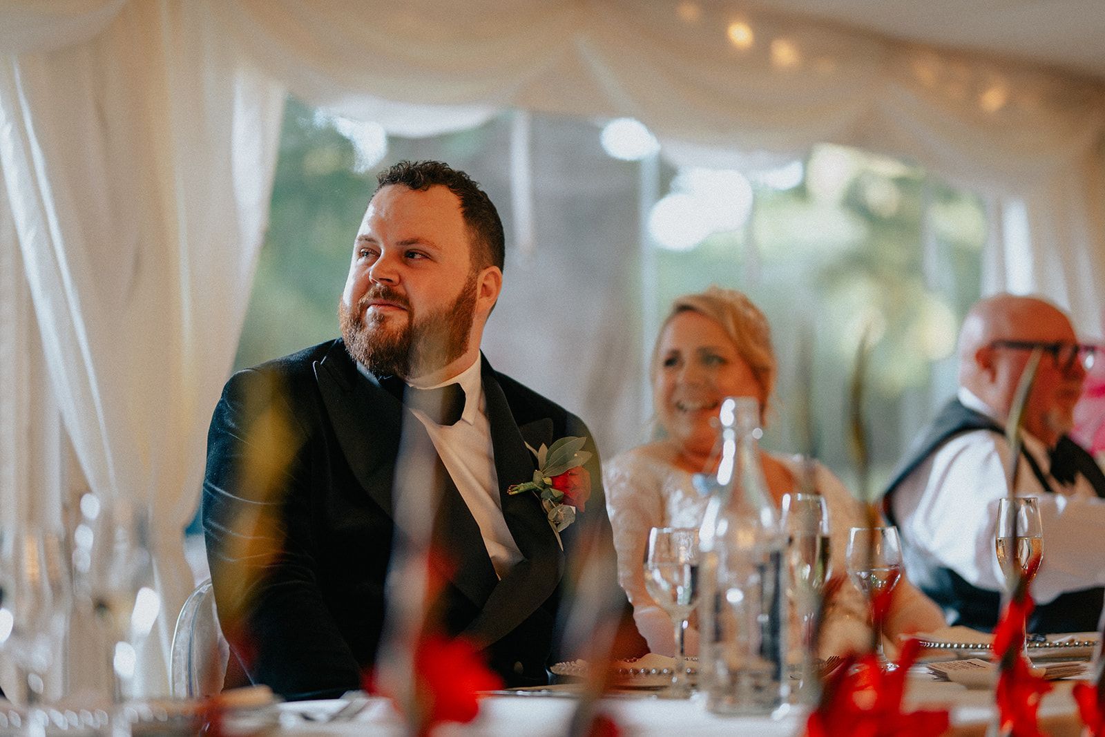 A man in a tuxedo is sitting at a table at a wedding reception.
