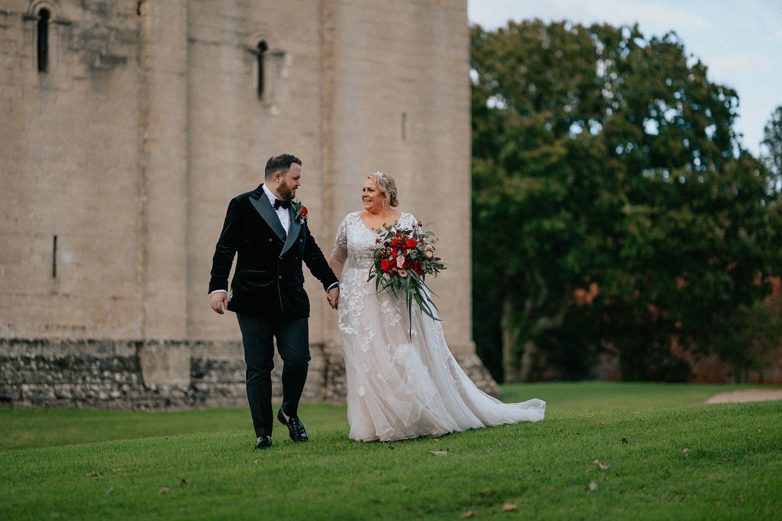 A bride and groom are walking in front of a castle holding hands.
