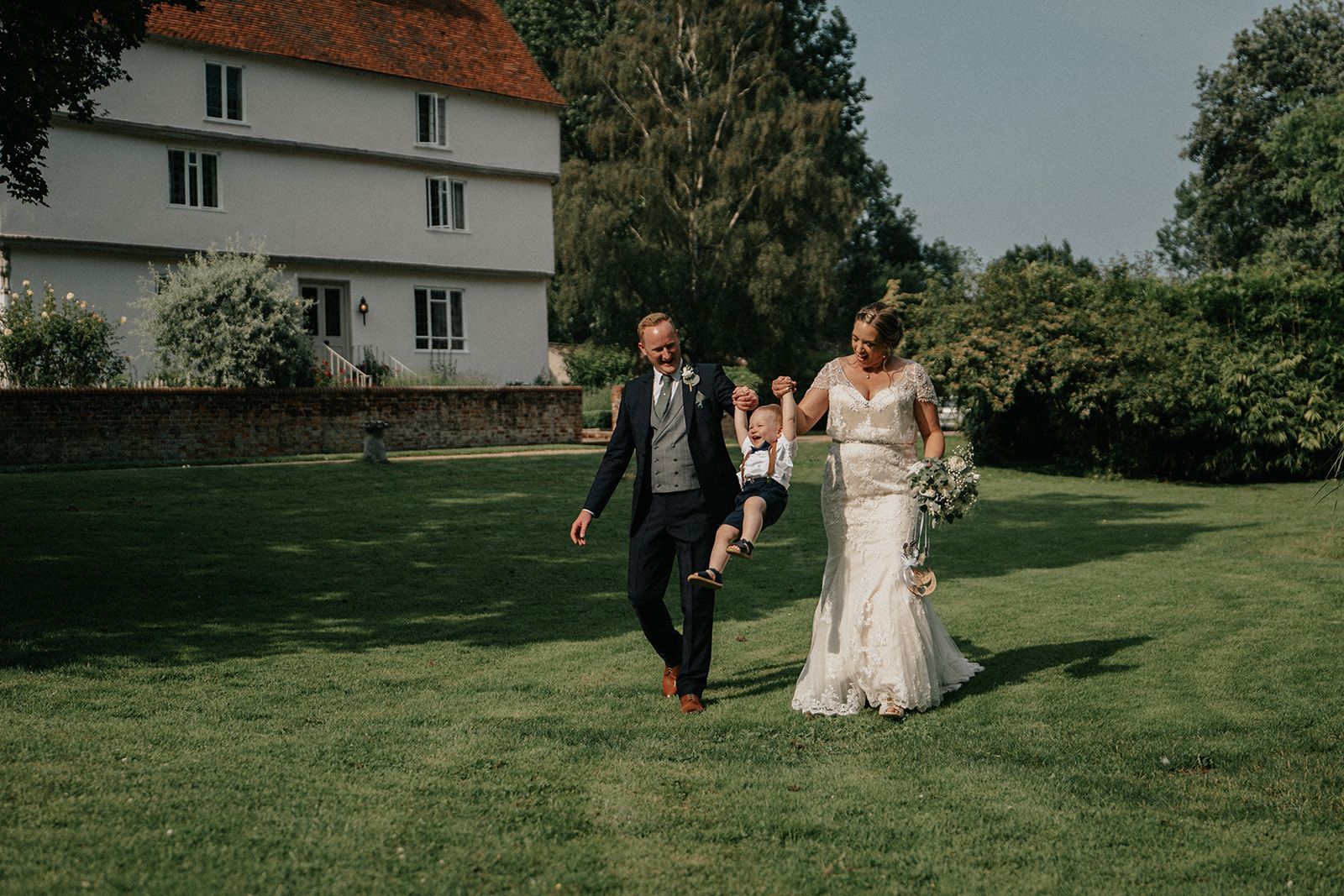 A bride and groom are walking through a grassy field.