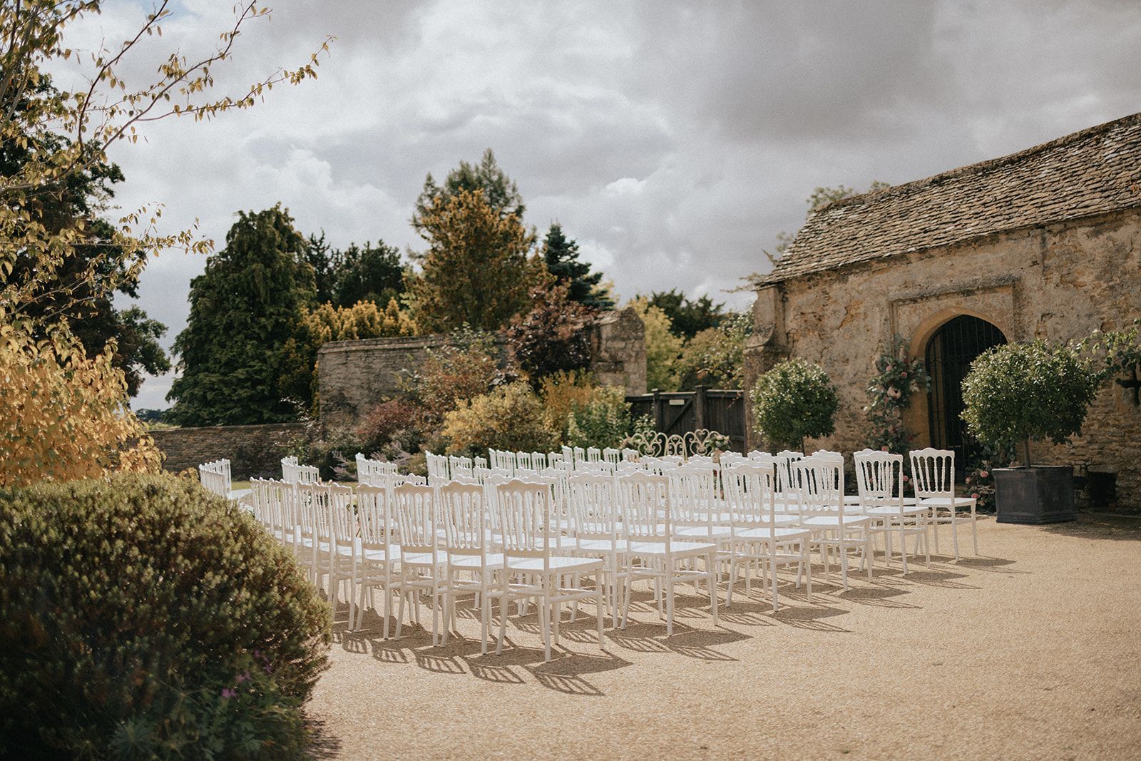A row of white chairs are lined up in front of a stone building.