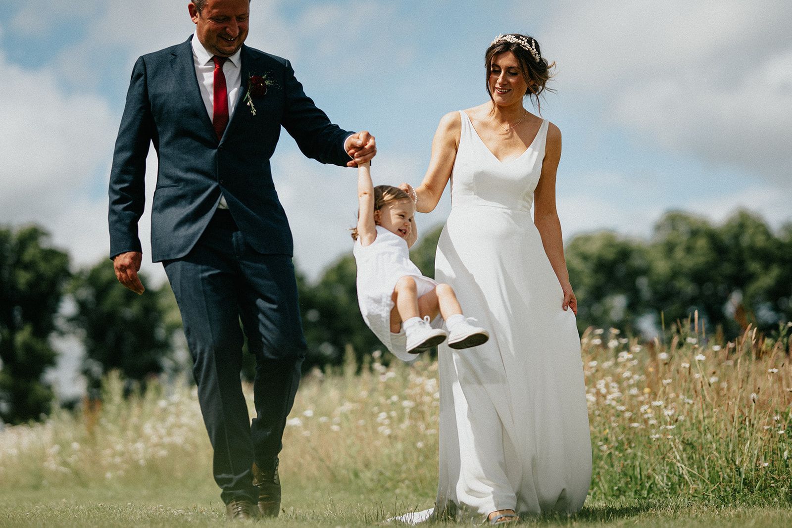 A bride and groom are holding hands with a little girl in a field.