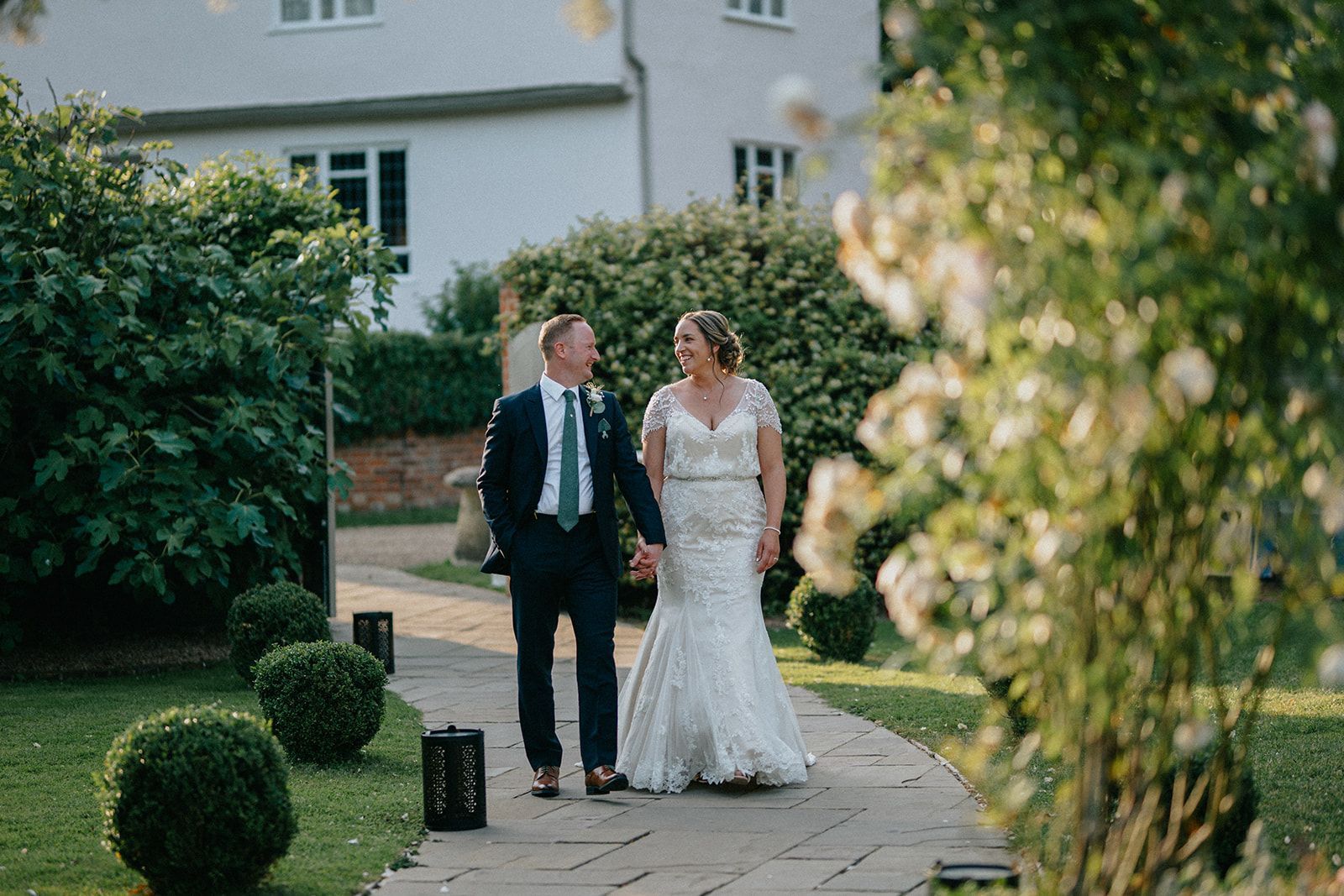 A bride and groom are walking down a path holding hands.