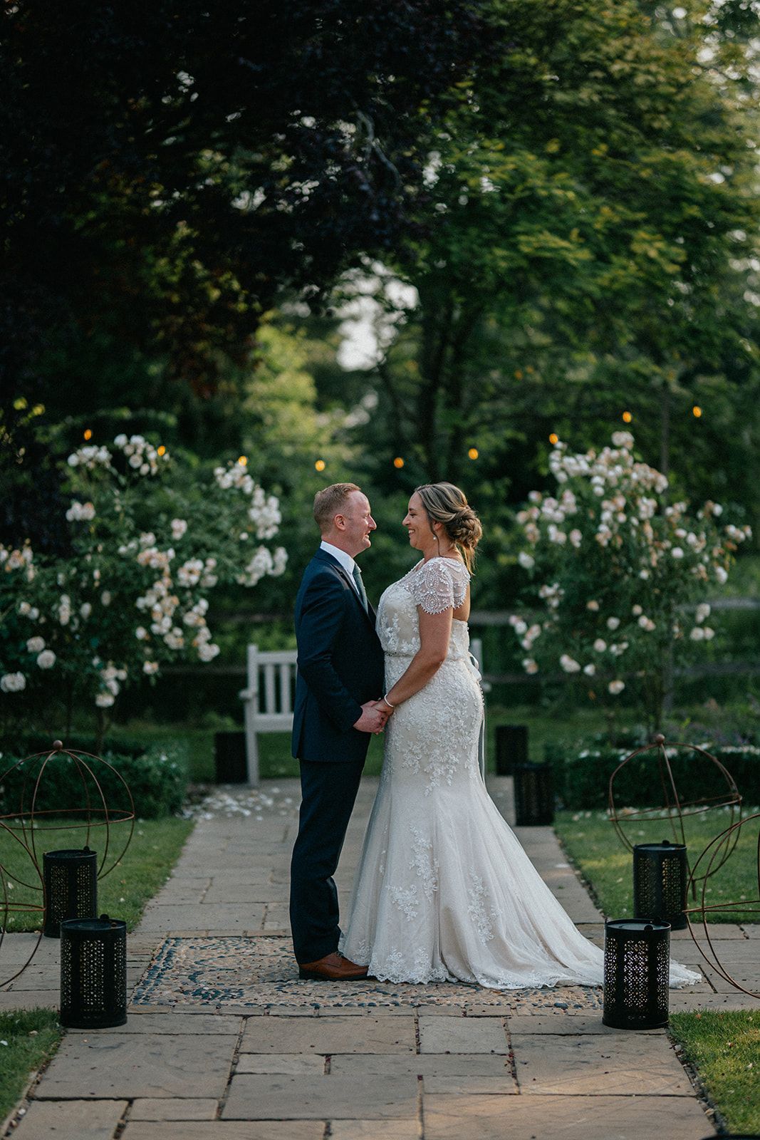 A bride and groom are holding hands and looking at each other in a garden.
