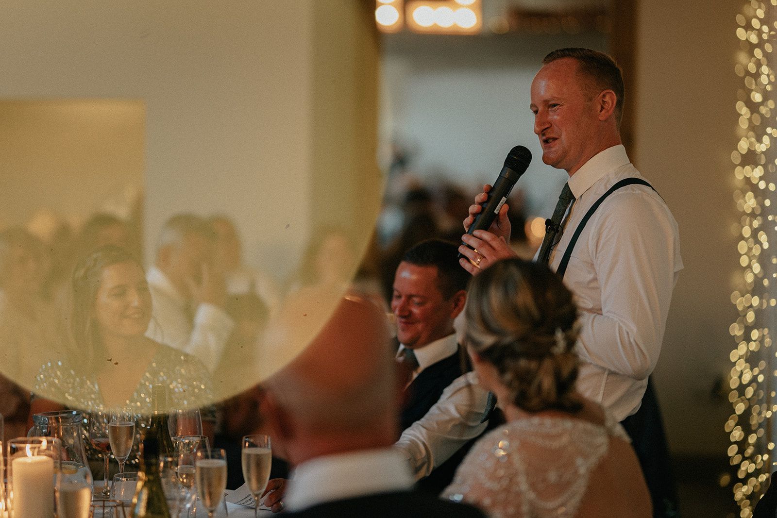 A man is giving a speech at a wedding reception while holding a microphone.