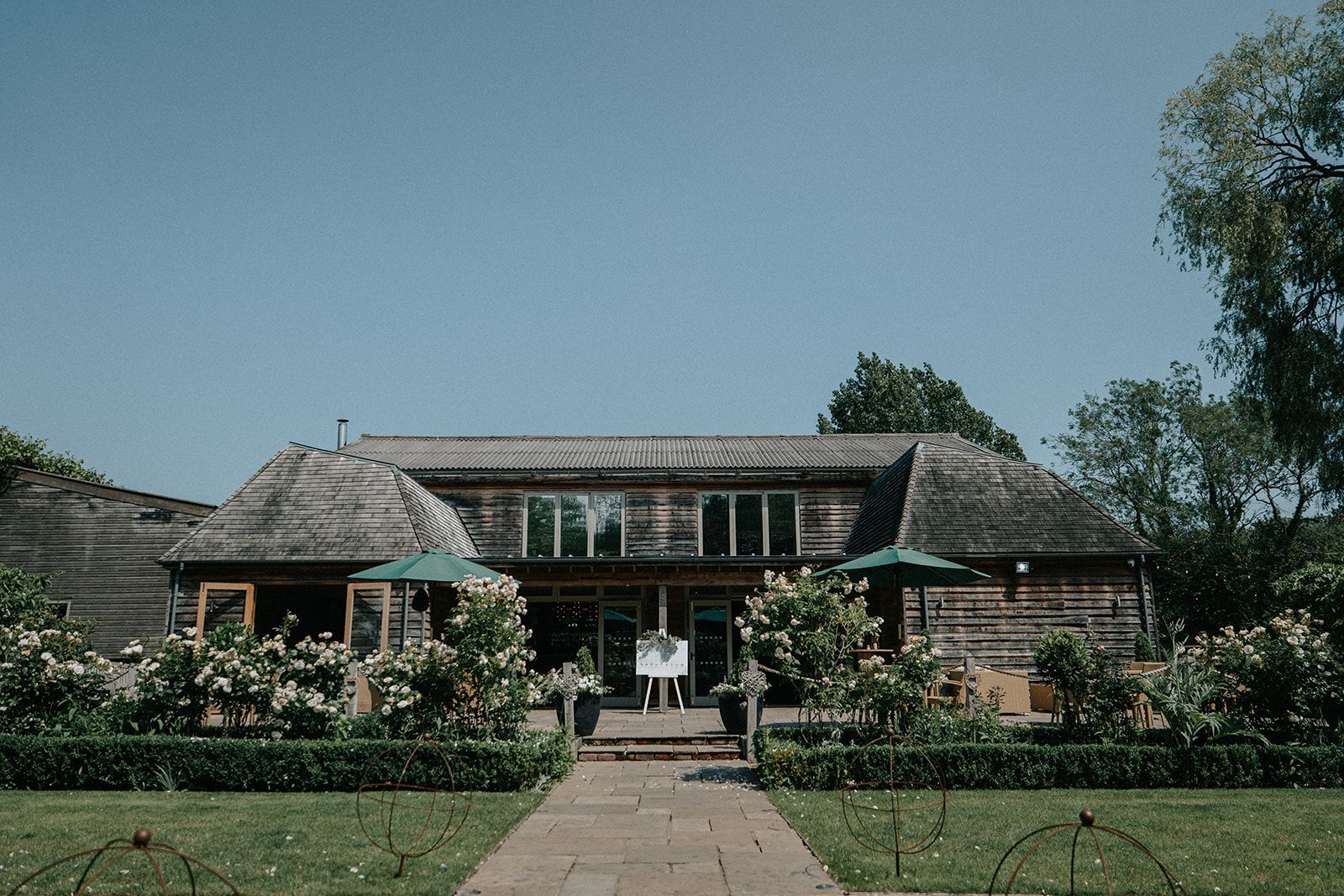 A large wooden house with a walkway leading to it surrounded by trees and bushes.