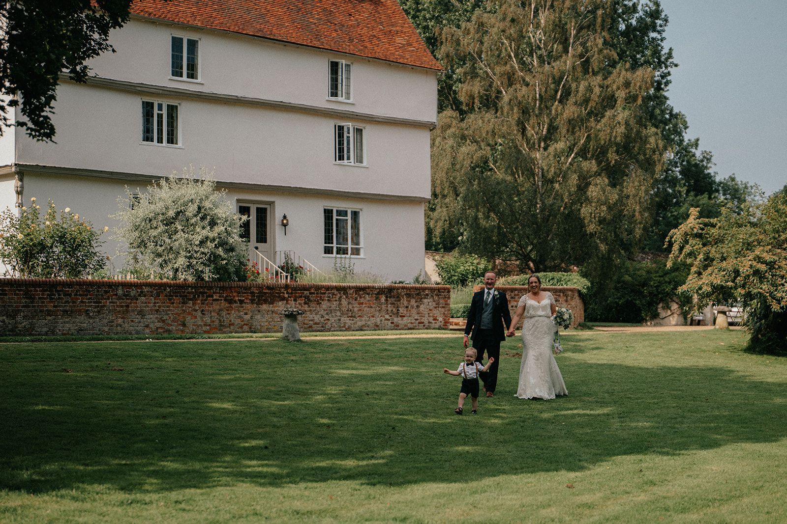 A bride and groom are walking with a child in front of a large white building.