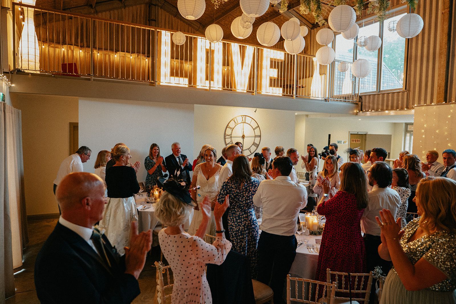 A large group of people are dancing at a wedding reception under a love sign.