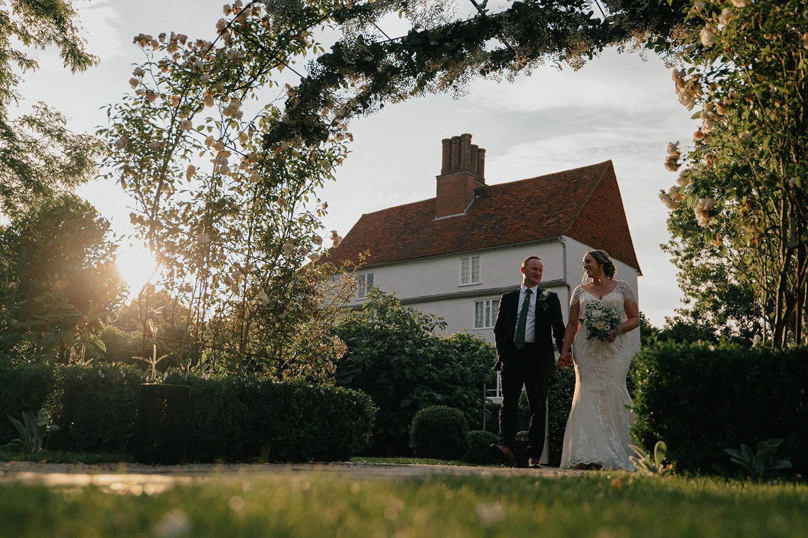 A bride and groom are holding hands in front of a large house.