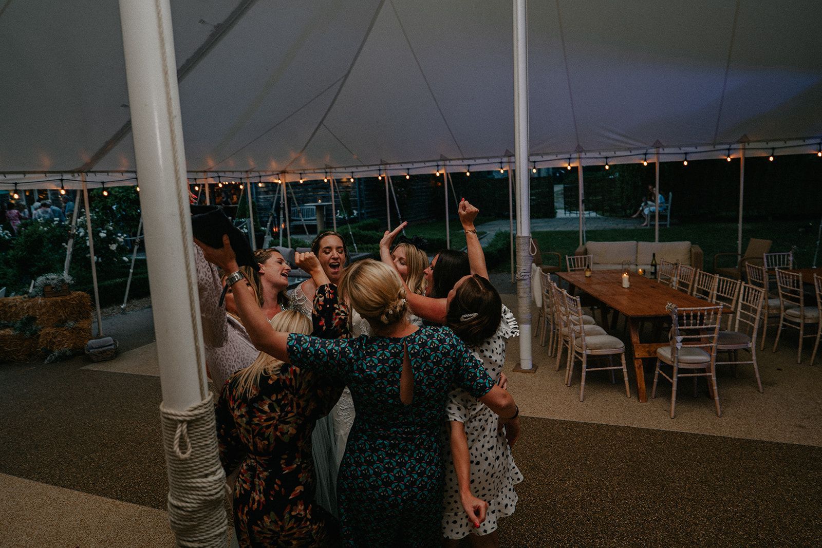 A group of people are dancing under a tent at a wedding reception.