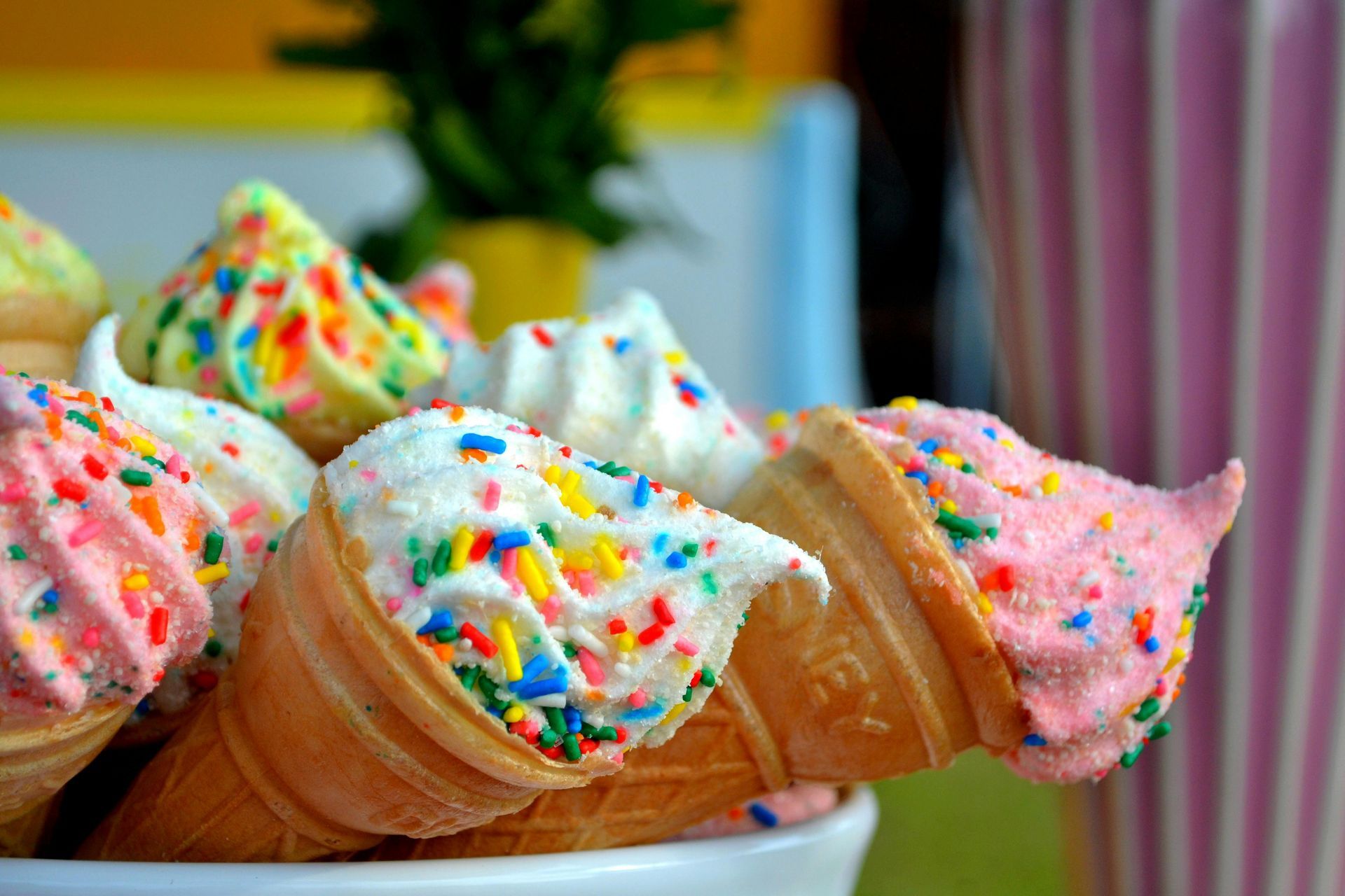 Ice cream cones with colorful sprinkles in a white bowl, next to a pink striped cup.