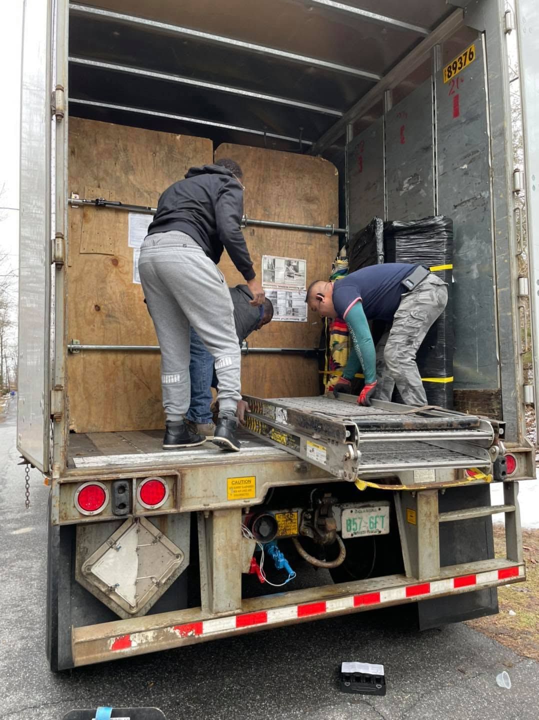 Two workers loading items into the back of a box truck with the ramp down.