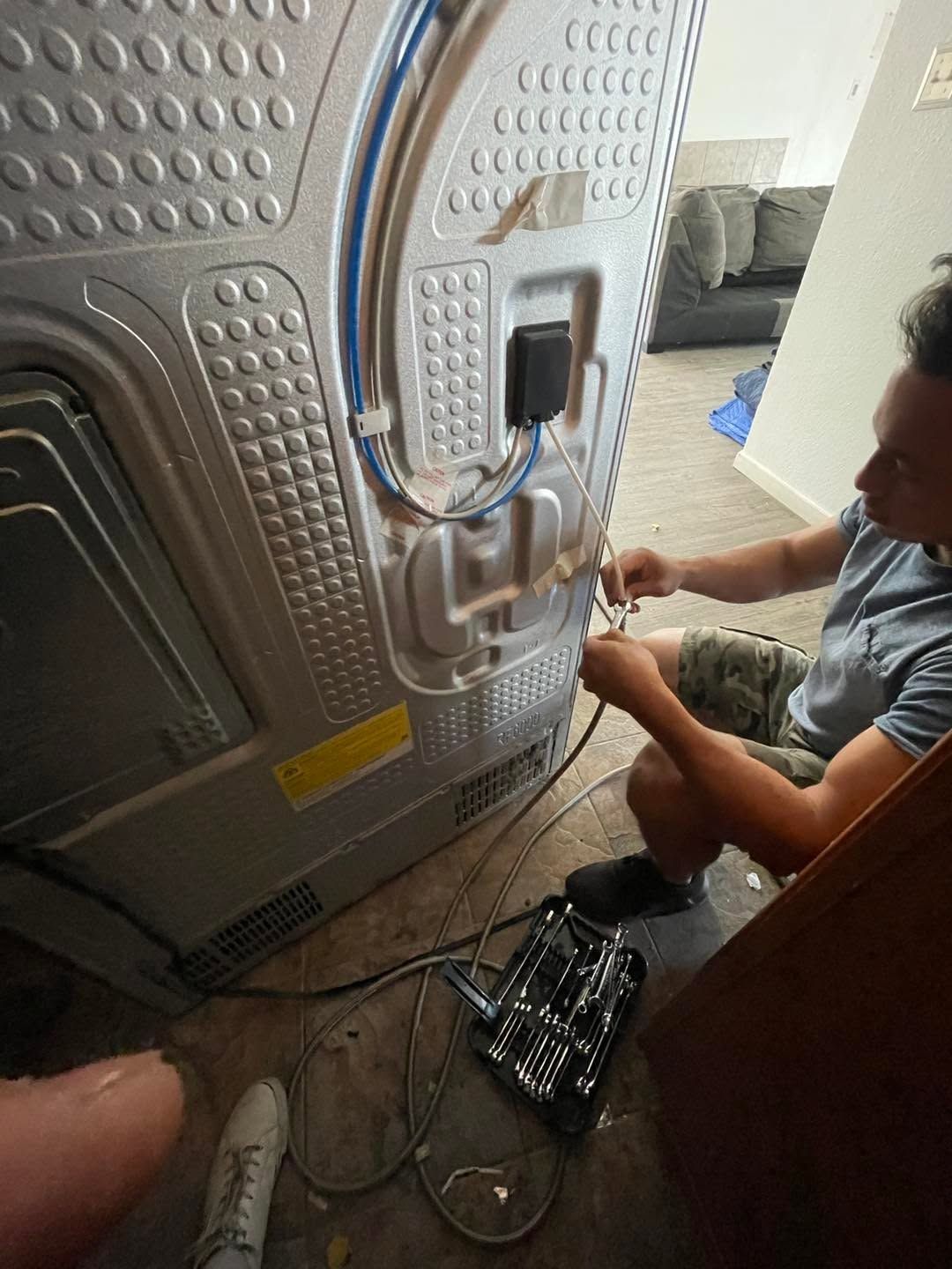 Person wiring cables to the back of a silver appliance on a floor, with tools nearby.
