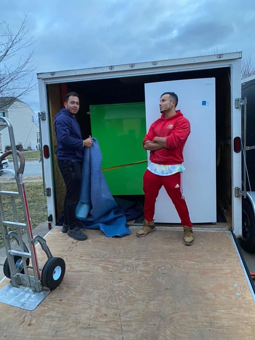 Two men unloading a truck, holding a blue tarp and a green panel on a ramp.