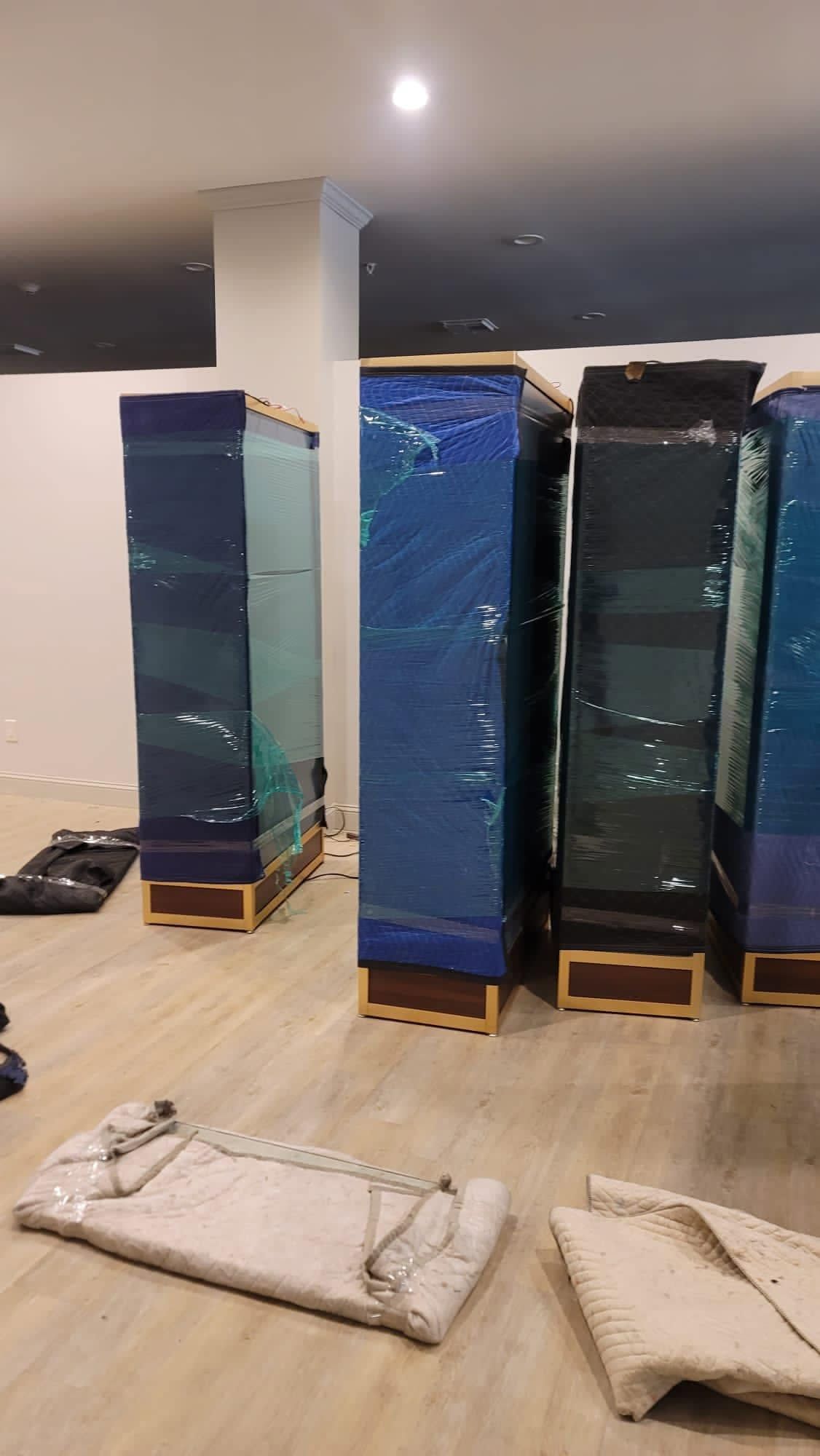 Covered blue cabinets and wrapped items in a room, suggesting movers or renovation in progress.