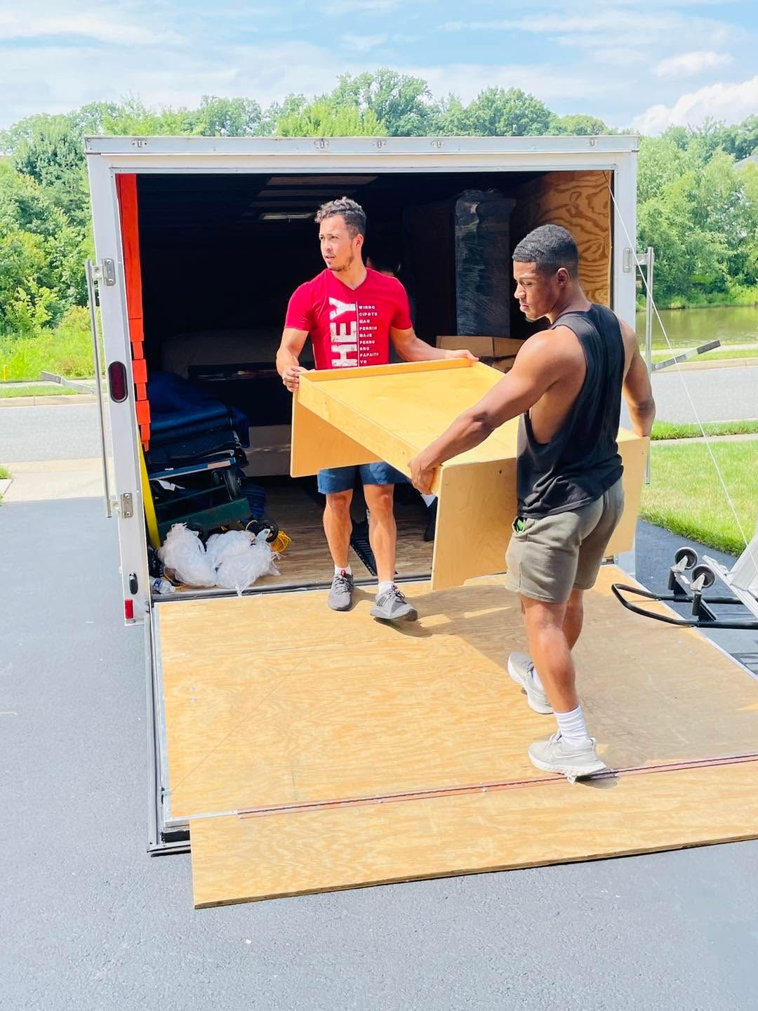 Two men loading a wooden board into a moving truck on a driveway.