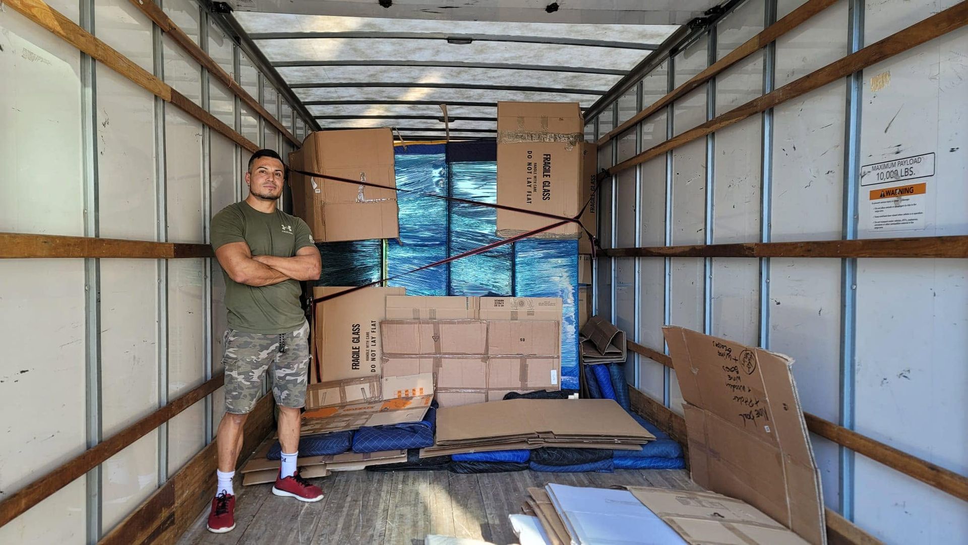Man standing in the back of a box truck beside stacked cardboard boxes and moving supplies
