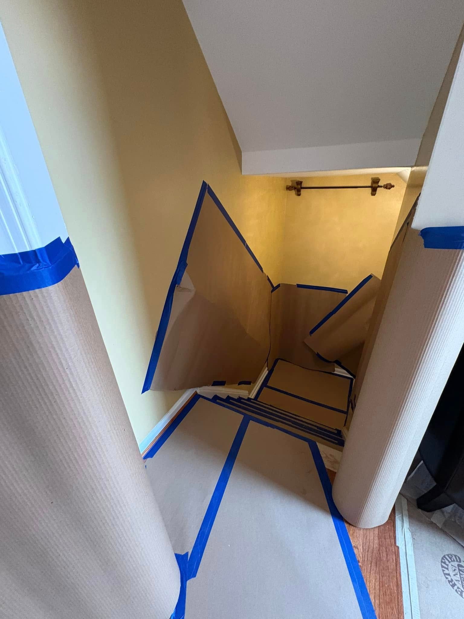 Stairwell with taped-off floor and a large open hole blocked by cardboard and tape, warning of construction hazard