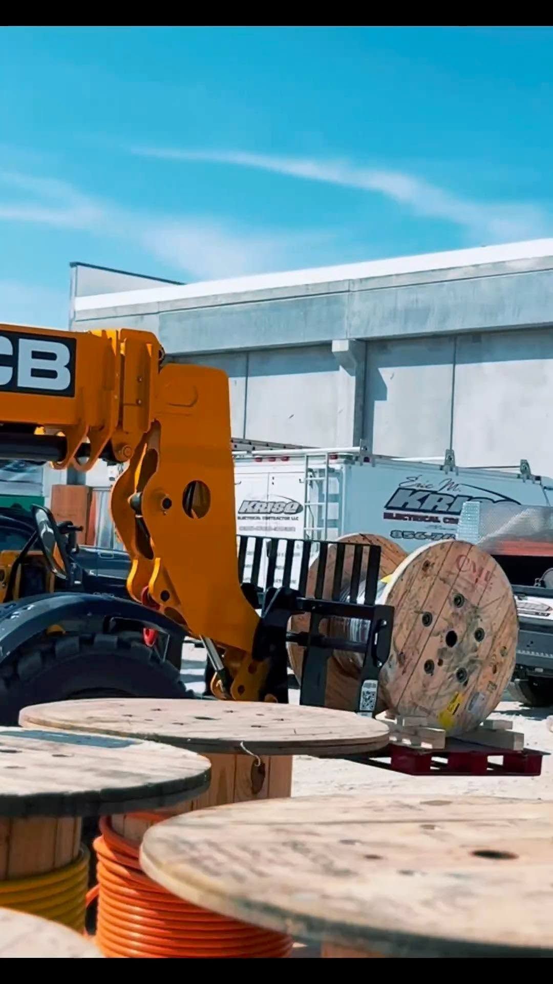 Orange construction equipment and wooden cable spools in a yard under a blue sky