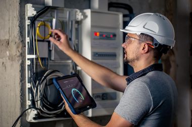 Technician inspecting electrical panel with a tablet in a utility room