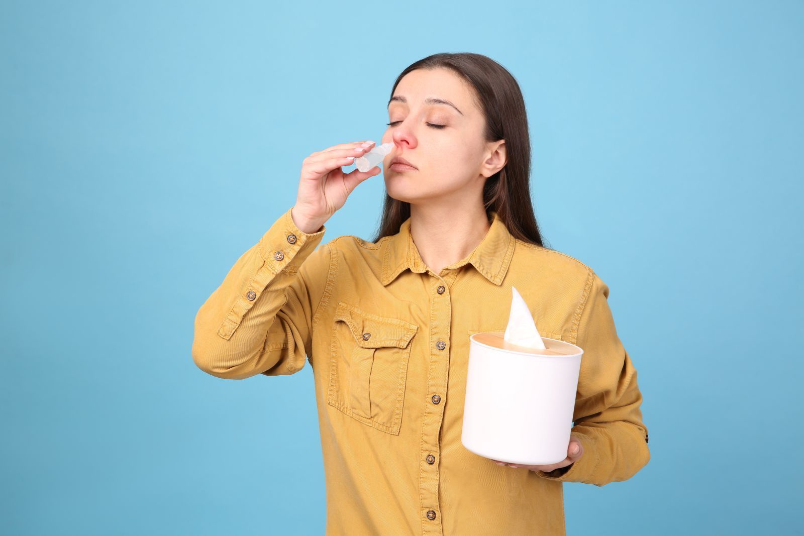 woman-using-nasal-spray-on-light-blue-background