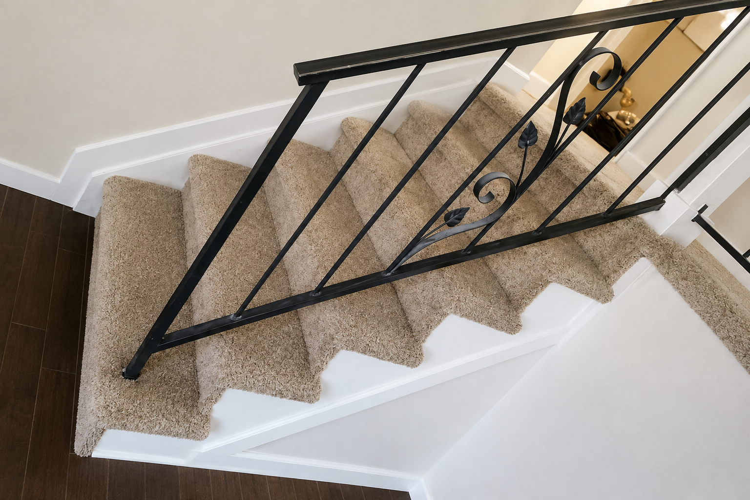 Carpeted staircase with black metal railing and white walls, viewed from above.