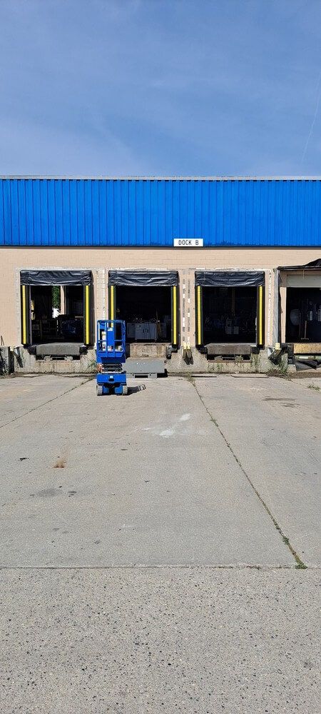 Warehouse loading docks with blue roof and blue lift. Concrete ground. Sunny day.