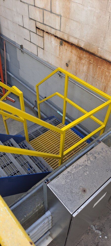Yellow safety railings and metal grating stairs. Industrial setting, concrete block wall.