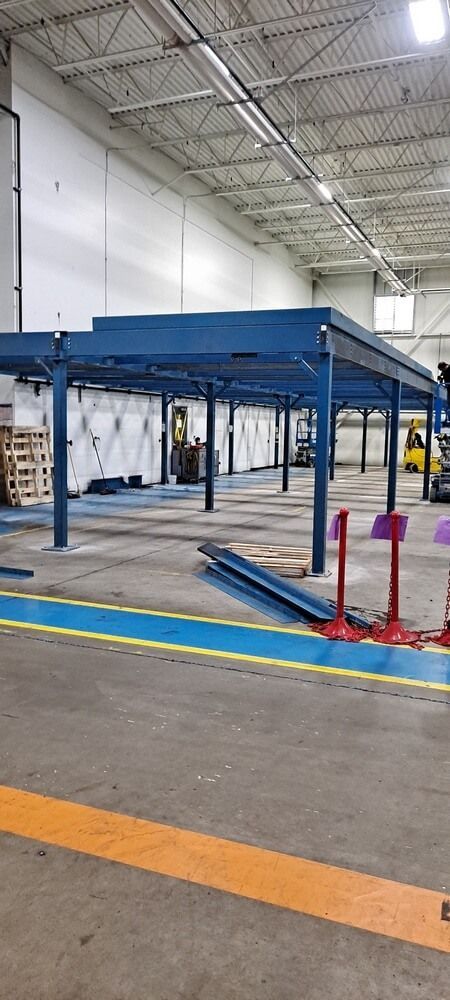 Blue metal structure in a warehouse with stacked items; blue, yellow floor lines; fluorescent lighting.