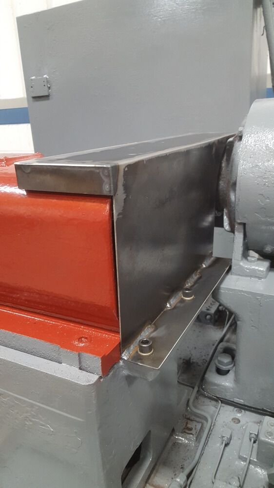 Metal enclosure covers a red and gray machine component. Bolts secure the enclosure to the base.